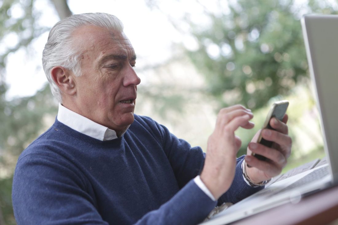 Older man in a navy sweater using a smartphone